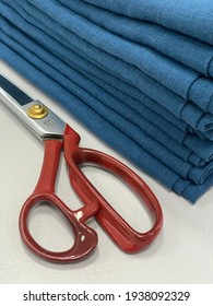 Sewing Process. Red Professional Scissors And Blue Linen Fabric On The Table. White Background. Handmade. Pile Of Linen Textile Products.