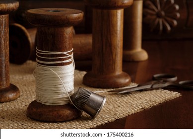 Sewing still life with antique thimble, scissors and wooden spools (from old textile mill - circa 1900). Antique sewing machine drawer in background. Macro with shallow dof.