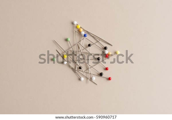 Sewing straight pins with heads of various\
colors on an off-white\
background