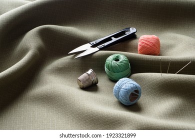 Sewing Supplies Lie On Draped Fabric, Close-up. Sewing Background. Colored Spools Of Thread, A Thimble, Needles On A Gray, Crumpled Fabric. Studio Concept. Tailoring, Fashion Designer.