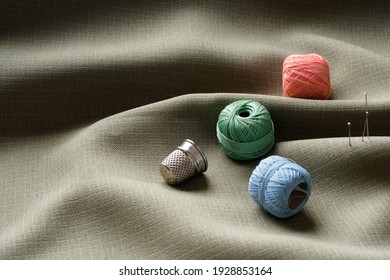 Sewing supplies lie on draped fabric, close-up. Sewing background. Colored spools of thread, a thimble, needles on a gray, crumpled fabric. Studio concept. Tailoring, fashion designer.