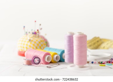 Sewing supplies on a white wooden table: sewing thread, scissors, a large spool of thread, pieces of cloth, needles,centimeter, buttons - Powered by Shutterstock