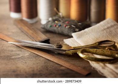 Sewing textile or cloth. Gold scissors pin cushion, and natural white fabric. Work table of a tailor. Shallow depth of field, Focus on scissors
