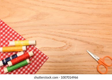 Sewing theme: bobbins, scissors and threads on a wooden background with plenty of copy space.
