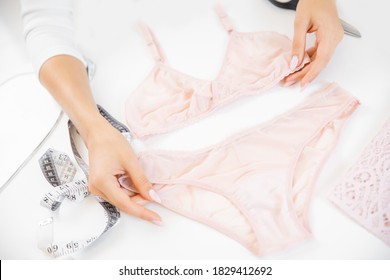 Sewing women underwear, bra and thong panties made of pink lace on table in hands of fashion designer.