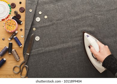 Sewing Workshop Or Fashion Designer At Work. Top View On Female Hand Ironing Cloth Square. Messy Table With Dressmaker Accessories, Copy Space