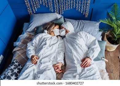 Sex during covid-19. Two people in protective suits and face masks, lying in bed and kissing through masks. Isolated at home because of quarantine for protection due to coronavirus. Safety comes first