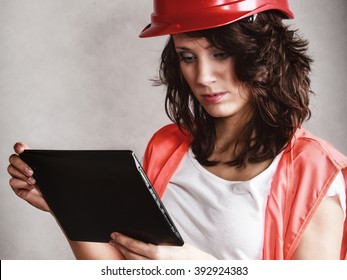 Sex Equality And Feminism. Sexy Girl In Workwear Safety Helmet And Orange Vest Using Tablet Touchpad Ipad On Gray. Young Attractive Woman As Construction Worker. Technology.