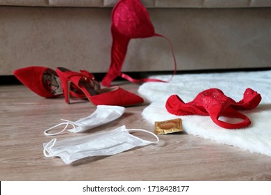 Sex on quarantine, two medical masks, red lace panties, bra and condom on the fur rug on a floor near sofa. Romantic night of passion, female lingerie