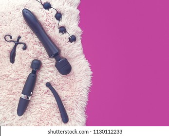 Sex toys (anal balls, vibrator, dildo and other) are on light sheep's fur. On the right is a blank space of fuchsia for text. The image is suitable for sex shop advertising