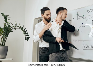 Sexual Harassment And Abuse At Work. A Male Boss Assaulting A Male Employee From Behind, Trying To Undress Him. The Subordinate Rejecting Unwanted Touching, The Expression Of Disgust On His Face. 