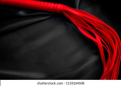 Sexual Kink And Erotic Games Concept With A Red BDSM Flogger Around Black Silk With Copy Space