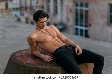 Sexually attractive man with naked torso wear in jeans, lying, looking down, posing on a roof.