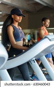 Sexy African American Slim Woman With Her Black Handsome Athletic Trainer On The Treadmill In Gym. Fitness Concept