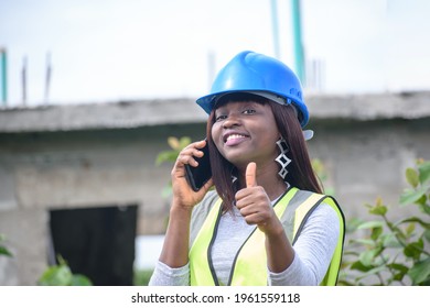 Sexy African Career Lady With Smart Phone Wearing Blue Safety Helmet Hard Hat With A Green Reflective Traffic Jacket As She Represents Professional Construction Workers And Architects 