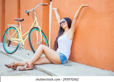 Sexy Awesome Asian Woman Sitting Near The Red Wall Background, There Is A Vintage City Bicycle. She Is Freedom And Raised Her Hands Up, Has Happy Vacation Travel