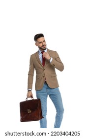 Sexy Bearded Man With Suitcase Looking To Side And Fixing Red Tie While Posing In Front Of White Background In Studio