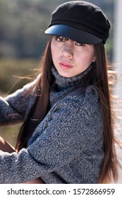 Sexy And Beautiful Asian Woman With The Sun In Her Long Black Hair Wearing A Grey Wool Sweater And A Black Military Cadet Hat