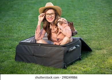 Sexy Beautiful Travel Woman Sitting In Huge Suitcase Over Green Grass Background. Happy Travel Woman Plan Vacation Concept, Copy Space