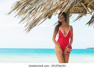 Sexy And Beautiful Woman Wearing Red Swimsuit Posing Under Old Thatch On Beach