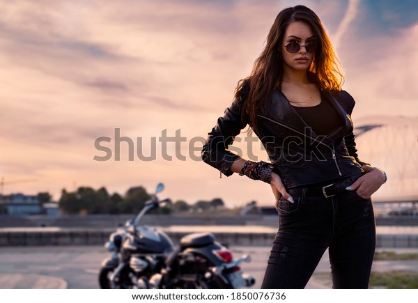 Sexy biker girl in leather jacket posing in\
sunset outdoors