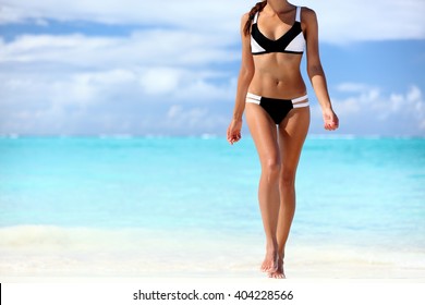 Sexy bikini body woman sun tanning relaxing on perfect tropical beach and turquoise ocean water. Unrecognizable model walking in fashion swimwear with smooth tanned skin and long lean legs.