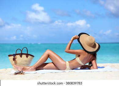 Sexy bikini woman tanning relaxing on beach. Suntan concept. Unrecognizable female adult from the back lying down with straw hat sunbathing under the tropical sun on Caribbean vacation.