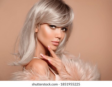 Sexy blond woman portrait. Blonde with beauty makeup, wavy hairstyle and manicured nails posing in fashion fur coat isolated on studio beige background.