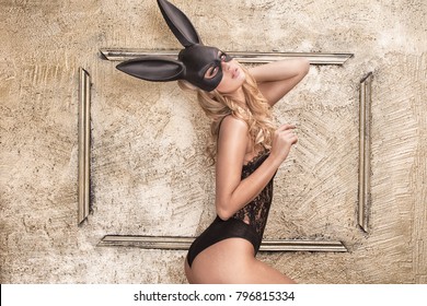 Sexy blonde beautiful woman posing in lace lingerie and black  bunny mask on gold background.