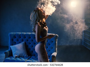 Sexy blonde in lingerie smokes electronic cigarette. The model vaping a vaporizer in the studio.