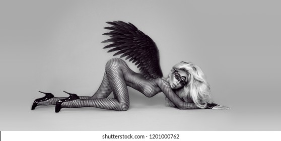 Sexy blonde model dressed in erotic lingerie and black wings. Woman with angel wings. Hot woman in bodystocking and high heels. Black and white photo.