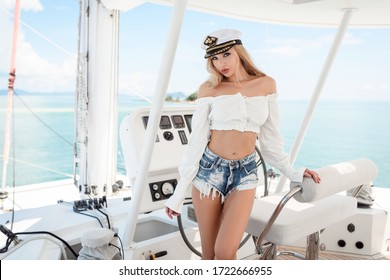  Sexy blonde Woman in a captain hat behind the wheel yacht, enjoying sea nature, active sailor girl, female driving luxury water transport, summertime concept