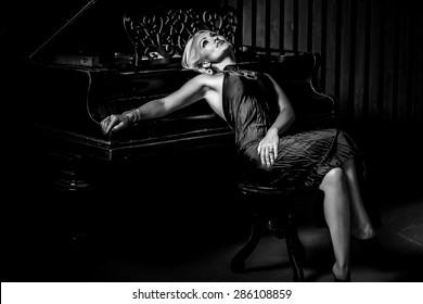 sexy blonde woman sitting near piano. Black and White Fashion studio portrait