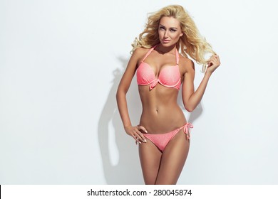 Sexy blonde woman wearing pink swimwear posing on white background. Perfect body