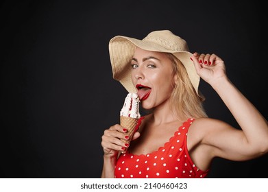 Sexy Blonde Woman Wearing Red One-piece Swimsuit With White Polka Dots, Eating Cold Ice Cream Cone Isolated Over Black Color Wall Background Studio. Summer Hotel Pool Sea Rest Sun Tan Concept