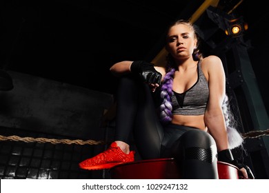 Sexy Boxer Girl Is Sitting On A Red Metal Barrel In The Ring. He Is Resting, Posing Before Training. Vintage Loft Gym Interior. Beautiful Braiding Kanekalon Pigtails Hairstyle, Wearing Gloves.