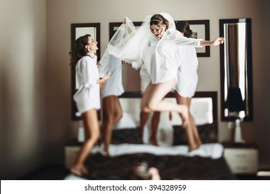 Sexy bride & bridesmaids jumping on bed before wedding