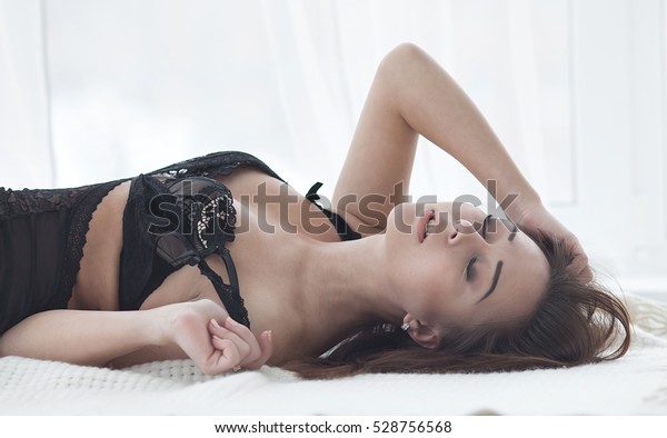ベッドに寝転がる黒い色っぽいランジェリーの中に 完璧な美しい体の形をしたセクシーなブルネット女性 の写真素材 今すぐ編集