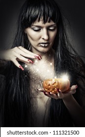 Sexy brunette woman witch making magic to pumpkin