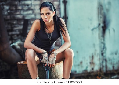 sexy brutal woman sitting in factory ruins and holding handgun