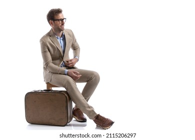 sexy businessman sitting on a chair, next to his briefcase, fixing his suit and wearing eyeglasses