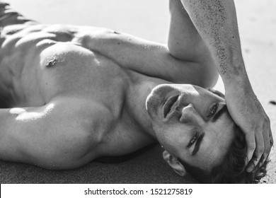 Sexy closeup portrait of handsome topless male model lying on the beach. Black and White.