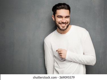 sexy fashion man model in white sweater, jeans and boots smiling against wall