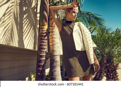 Sexy Fashionable Young Woman In Glitter Dress Posing Under Palm Tree, High Heels, Short Hair. Fashion Summer Photo. Bright Colors