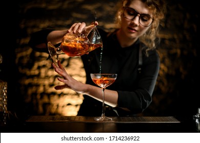 Sexy Female Bartender In Black Shirt Gently Pours Drink From Mixing Cup With Strainer Into Glass