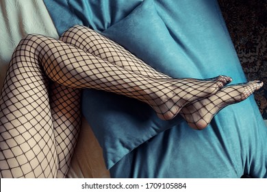Sexy female long legs, black fishnet stockings, on sofa, indoors