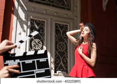 Sexy girl behind a Clapper board. Film-making or film production concept , photo set of young model on vintage building background. Red lips, black hat. dramatic game