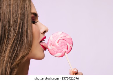 Sexy Girl Eating Lollipop. Beauty Glamour Model Woman Licking Sweet Colorful Lollipop Candy, Close-up. Closeup Mouth And Tongue. Seductive Lips, Perfect Fashion Make-up, Pink Color Lipstick