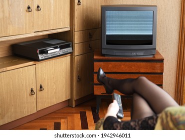 Sexy Girl Sitting In A Vintage Armchair Watches Old TV.Old Black TV With Clutter On The Screen And VCR Against Old Furniture From The 1980s And 1990s. Design In The House In The Style Of The 1980s.