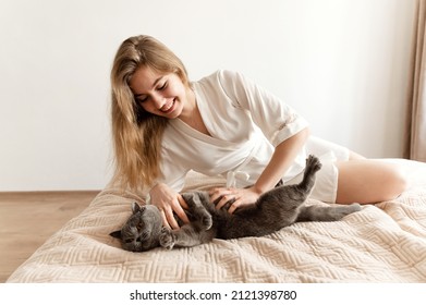 A Sexy Girl In Thin Pajamas Sits On The Bed And Holds A Beautiful Scottish Cat. Sexy Girl At Home In Pajamas On A Bed With A Pet